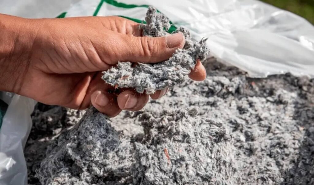 To zdjęcie przedstawia rękę trzymającą kępę szarego, włóknistego materiału. Jest to prawdopodobnie izolacja celulozowa, która często używana jest do ocieplenia budynków.